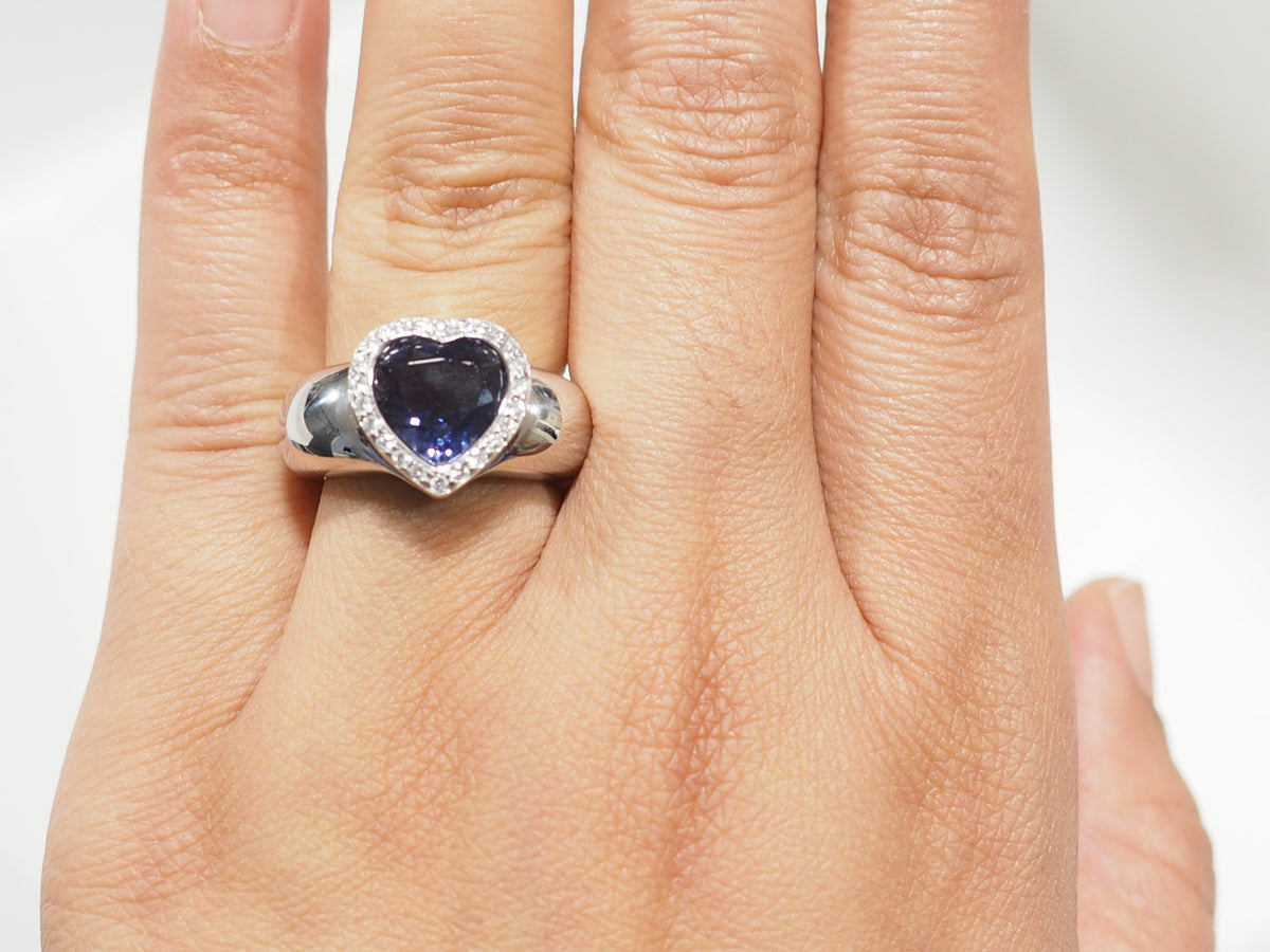Bague L'Aurore Poiray en or blanc avec tanzanite en forme de cœur entourée de diamants portée au doigt