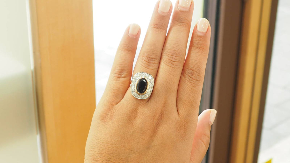 Bague pompadour L'Aurore en or jaune et platine avec un saphir ovale entouré de diamants portée sur un doigt