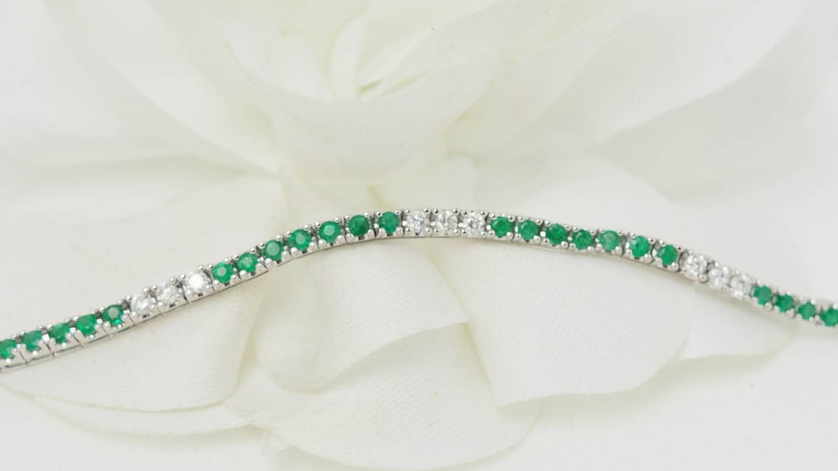 Bracelet rivière L'Aurore en or blanc 18kt serti d'émeraudes et de diamants taille brillant sur fond floral blanc