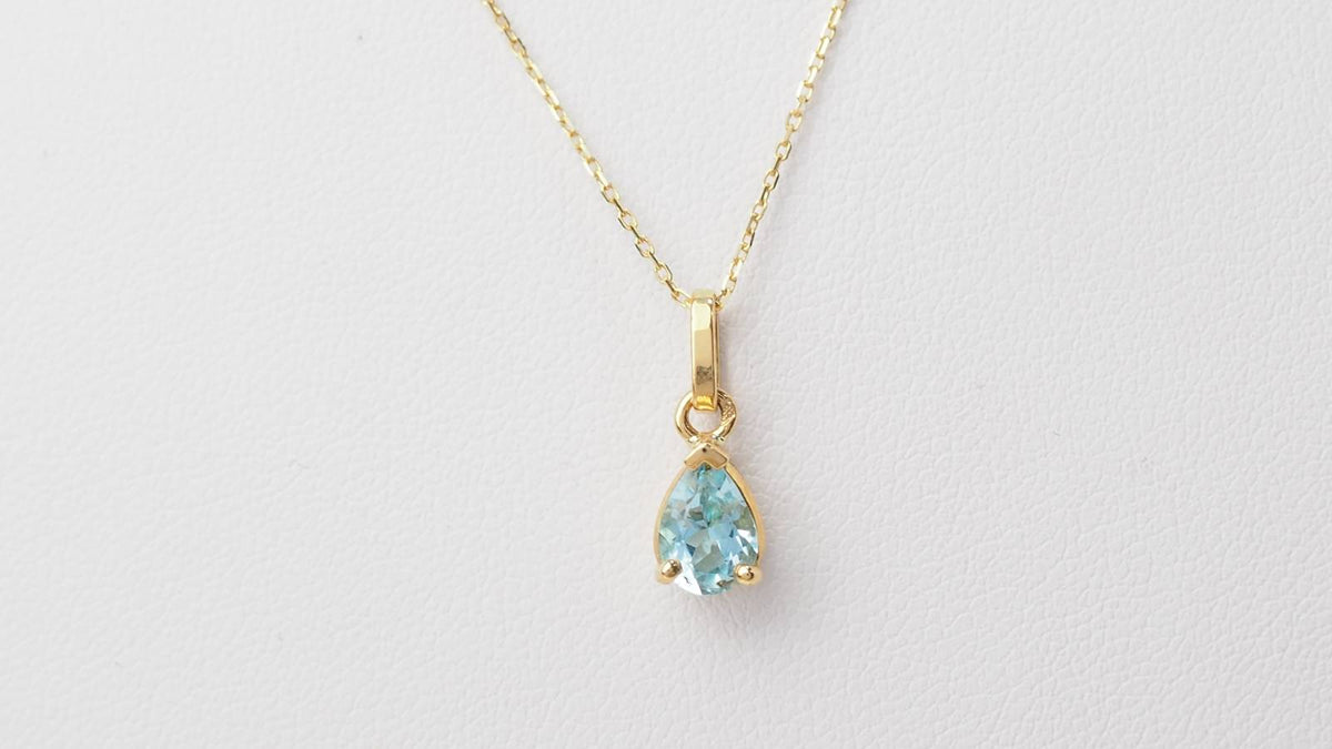 Collier solitaire L'Aurore en or jaune 18k avec une topaze bleue taille poire sur une fine chaîne maille forçat