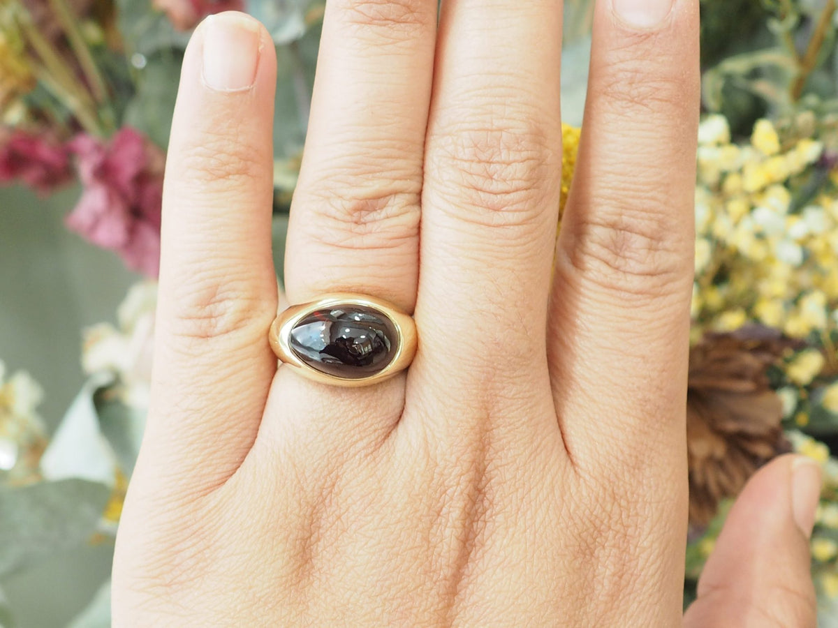 Bague vintage L'Aurore Pomellato en or jaune 18kt ornée d'un grenat cabochon porté sur un doigt